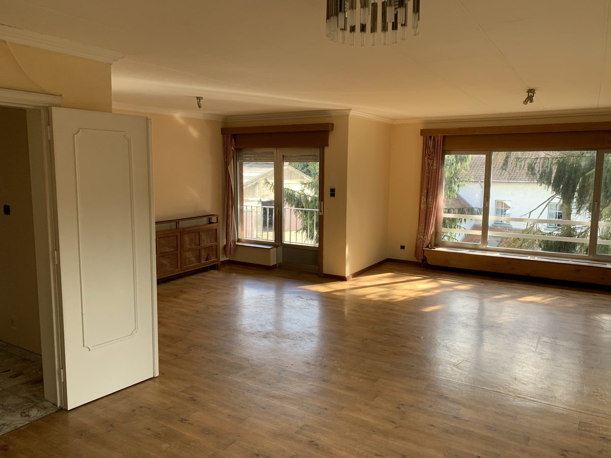 Séjour vide avant occupation : parquet, deux baies avec radiateurs en allège, une porte intérieure ouverte.